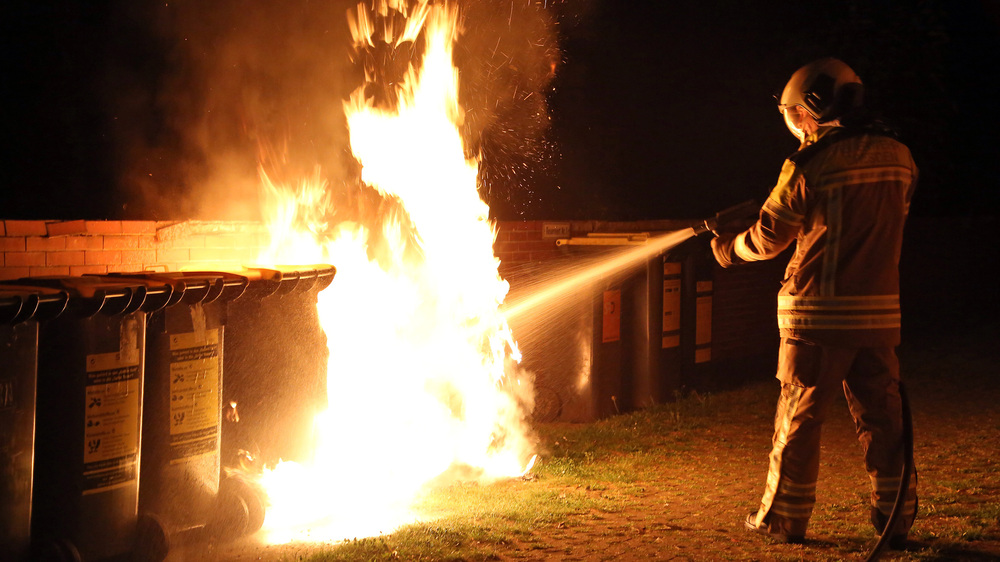 © Roland Halkasch Symbolbild: Ein Feuerwehrmann löscht einen brennenden Müllcontainer
