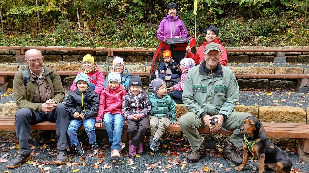 Zum Abschluss ihrer Entdeckungstour durch die Waldhusche nahmen Frank Strohbach von der Nationalparkwacht (l.), die Kinder der Hinterhermsdorfer Kindertagesstätte „Haus des Gastes“, ihre Betreuerinnen Sabine Petters (h. m.) und KiTa-Leiterin Kathrin Krause-Nedon (h. r.) sowie Oberförster Matthias Protze (r.) in den Publikumsreihen der Naturbühne Platz. Hier gibt es in der Saison auch kulturelle Veranstaltungen. Foto: K. Partzsch