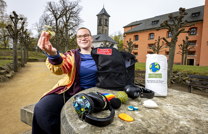 Besucherin Lisa Hösel testet den Sensory Bag auf der Festung Königstein. Zum Inhalt des Rucksacks gehören unter anderem ein Akupressurring, ein Fidget Spinner, geräuschdämpfende Kopfhörer und weitere sensorische Hilfsmittel für einen reizarmen Museumsbesuch. Foto: Marko Förster/ Festung Königstein